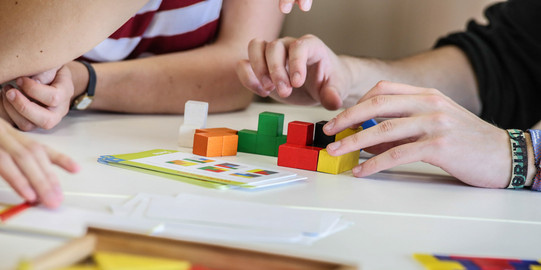 Kunststoffplättchen-Holzwürfel Zwei Personen bauen mit kleinen bunten Holzwürfeln.