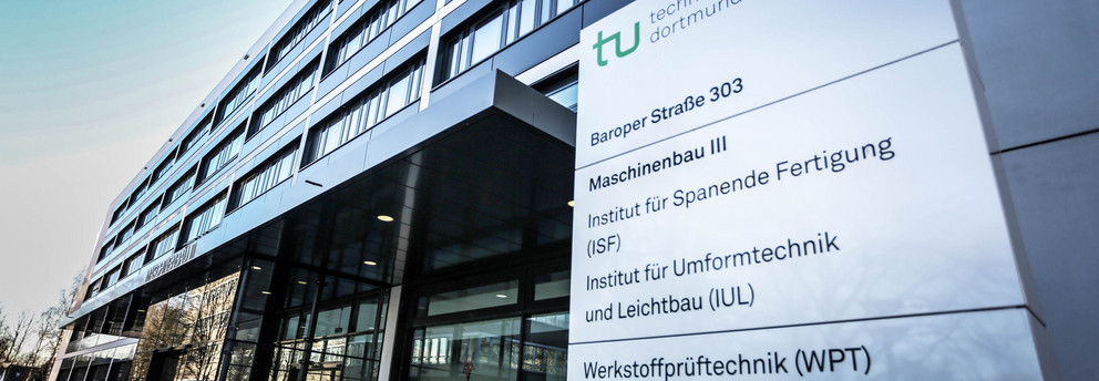 Maschinenbau-Gebäude III Maschinenbau-Gebäude III: Ein modernes grau-schwarzes Gebäude aus Glas mit Vordach, seitlich von unten fotografiert. Rechts vor dem Gebäude ein Schild mit der Aufschrift "Technische Universität Dortmund, Baroper Straße 303, Maschinenbau 3" und weiteren Instituten und Einrichtungen.