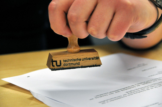 Symbolbild Stempel Nahaufnahme einer Hand, die einen Stempel der TU hält.