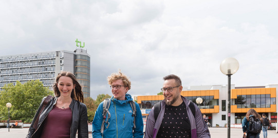 Studierende laufen über die Mensabrücke Drei Studierende laufen über die Mensabrücke und unterhalten sich.