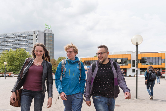 Studierende laufen über die Mensabrücke Drei Studierende laufen über die Mensabrücke und unterhalten sich.