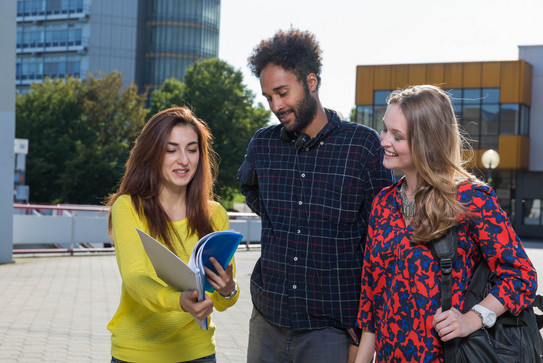 Studierende am Campus Nord Drei Studierende stehen zusammen auf einem Platz vor zwei Gebäuden.