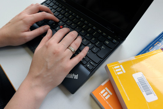 Lernen mit dem Laptop Eine Studentin tippt an einem Laptop und gelbe Bücher legen daneben.