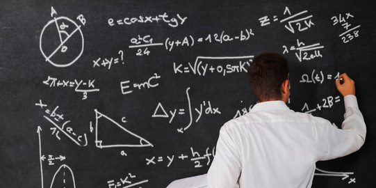 Rückenansicht-Tafel Ein Mann steht vor einer Tafel und rechnet.