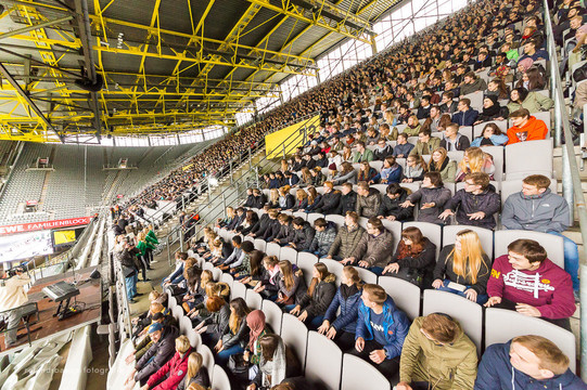 Erstsemesterbegrüßung Studierende des ersten Semesters sitzen bei der Erstsemesterbegrüßung auf den Rängen im Stadium und schauen seitlich einem Showact zu.